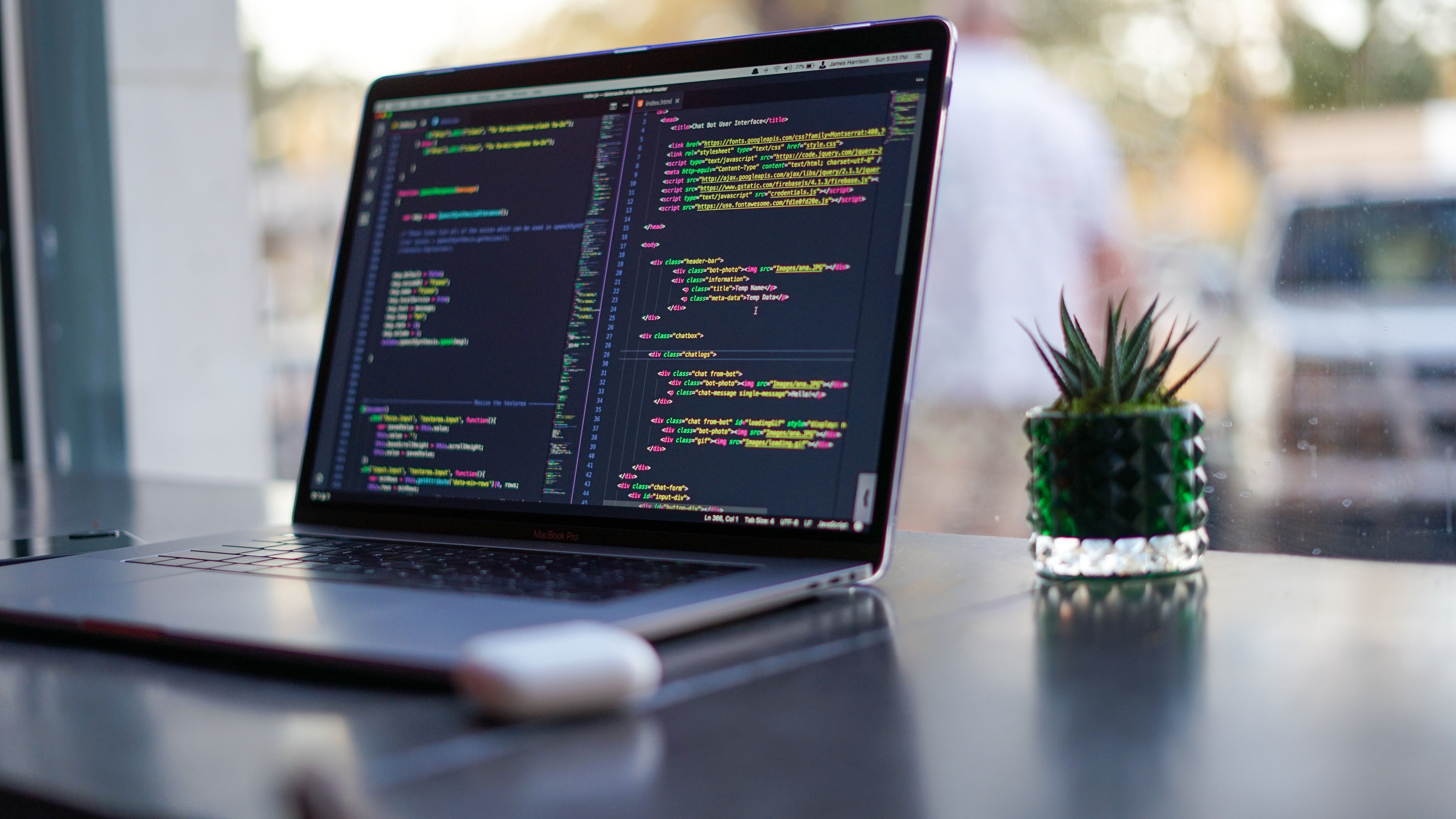 Photo of a MacBook on a table facing a window, there are AirPods and a faux plant in view, code is on the screen.