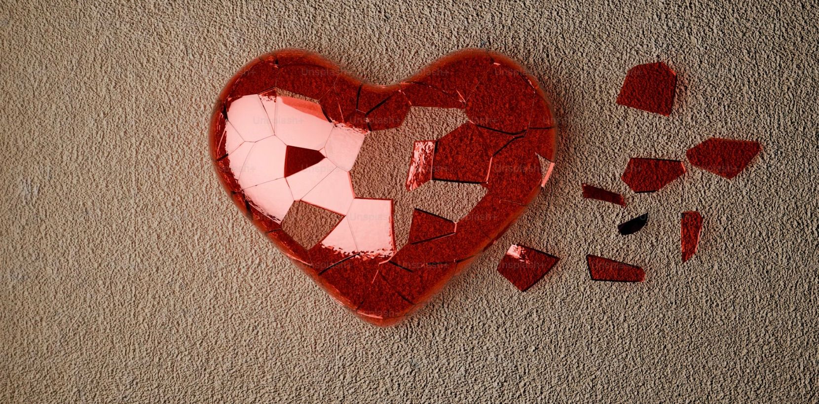 A heavily fractured red heart. While the main form remains mostly intact on the left, the right side has broken apart, with several sharp, jagged shards scattered away from the main body.