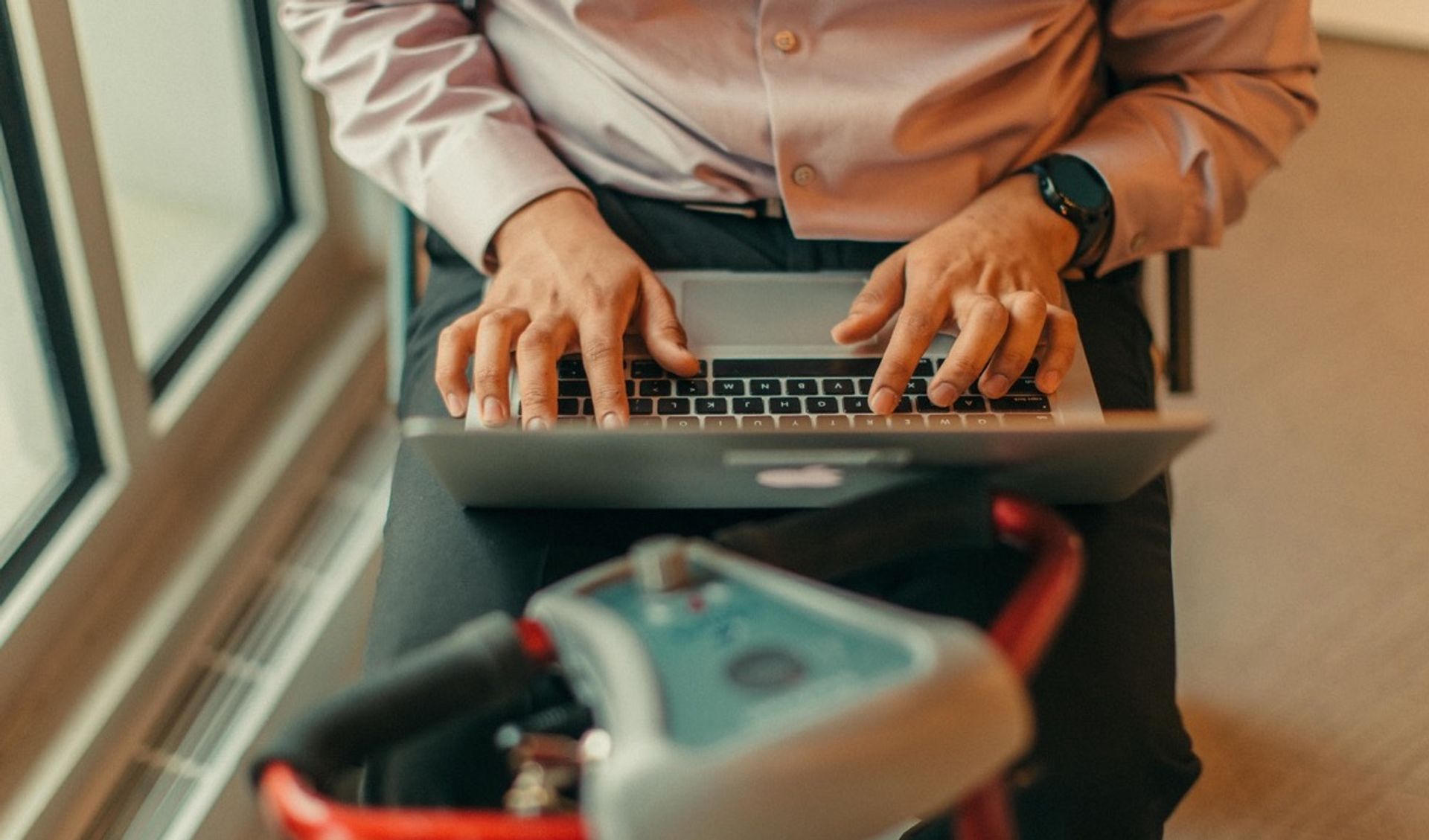 Close up shot of a man (possibly south asian) typing on laptop on his motorised scooter